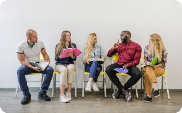 a group of 5 men and women sitting in chairs with notebooks talking to eachother
